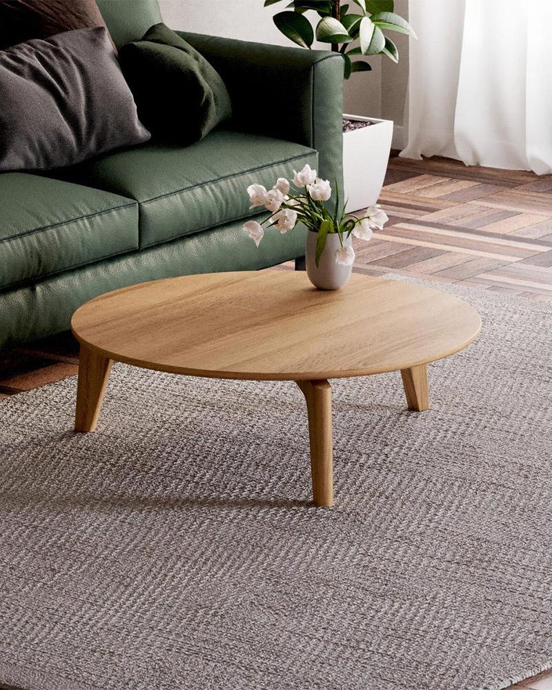 Scandinavian round solid oak coffee table with thick top and stable tripod base in a bright, modern apartment
